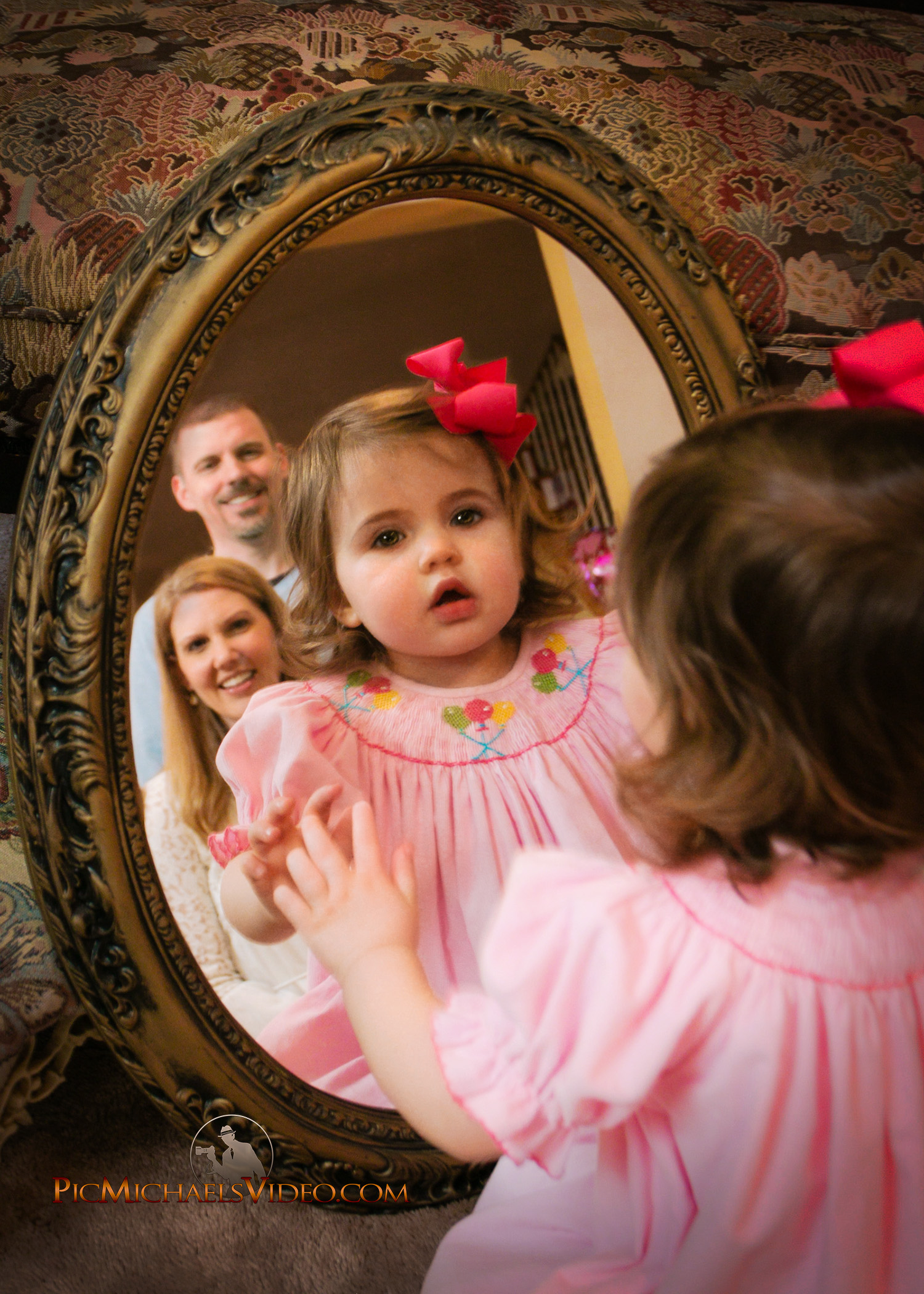 A cute baby looking at her parents in mirror.